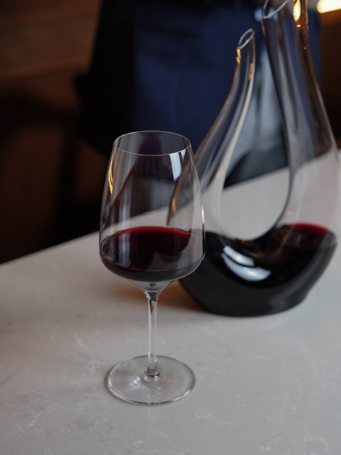 A sophisticated glass of red wine beside a sleek decanter on a marble table.
